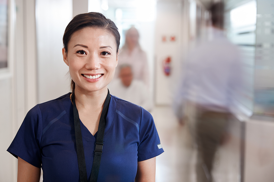 Nurse wearing dark blue scrubs standing in a hospital smiling at the camera.
