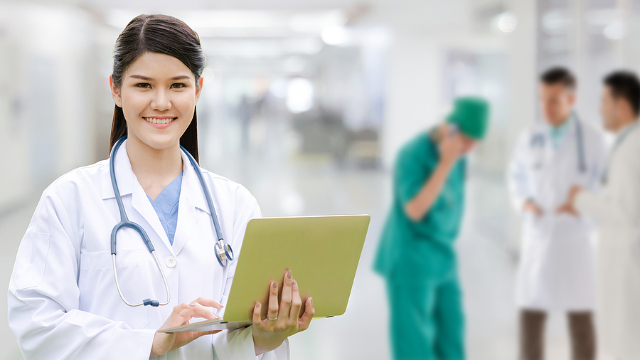 Medical assistant standing in a hospital holding a laptop.