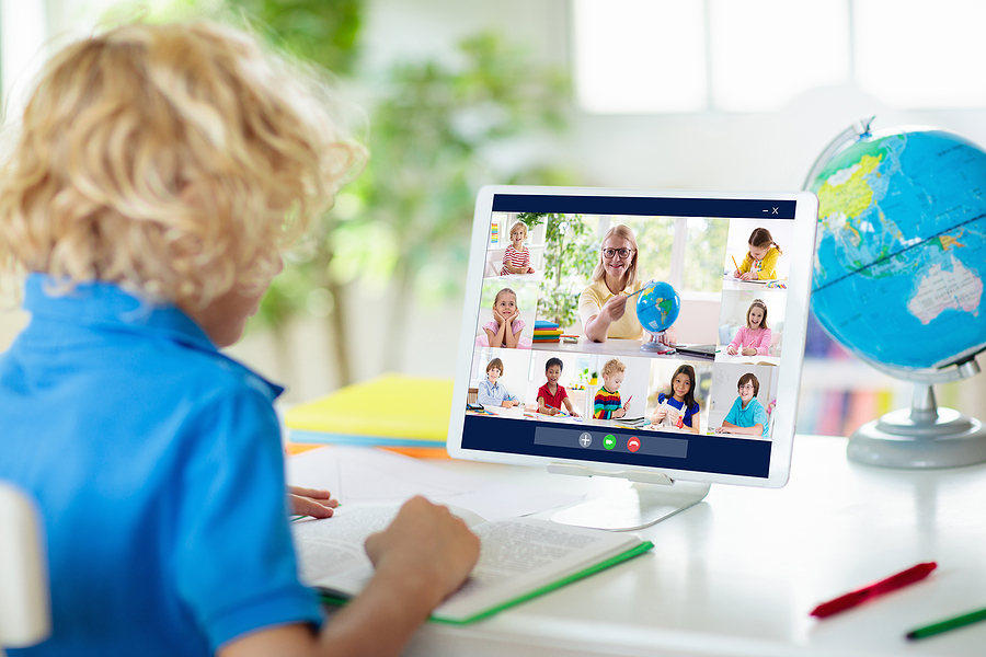 Young student sitting in front of a virtual class meeting with teacher and classmates.