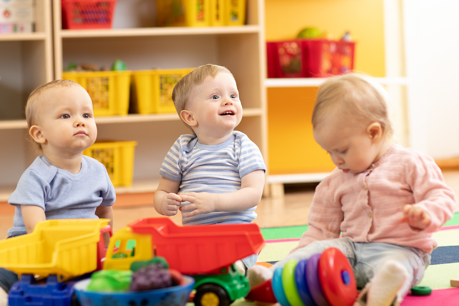 Three happy children playing with toys in a bright and cheerful childcare classroom.