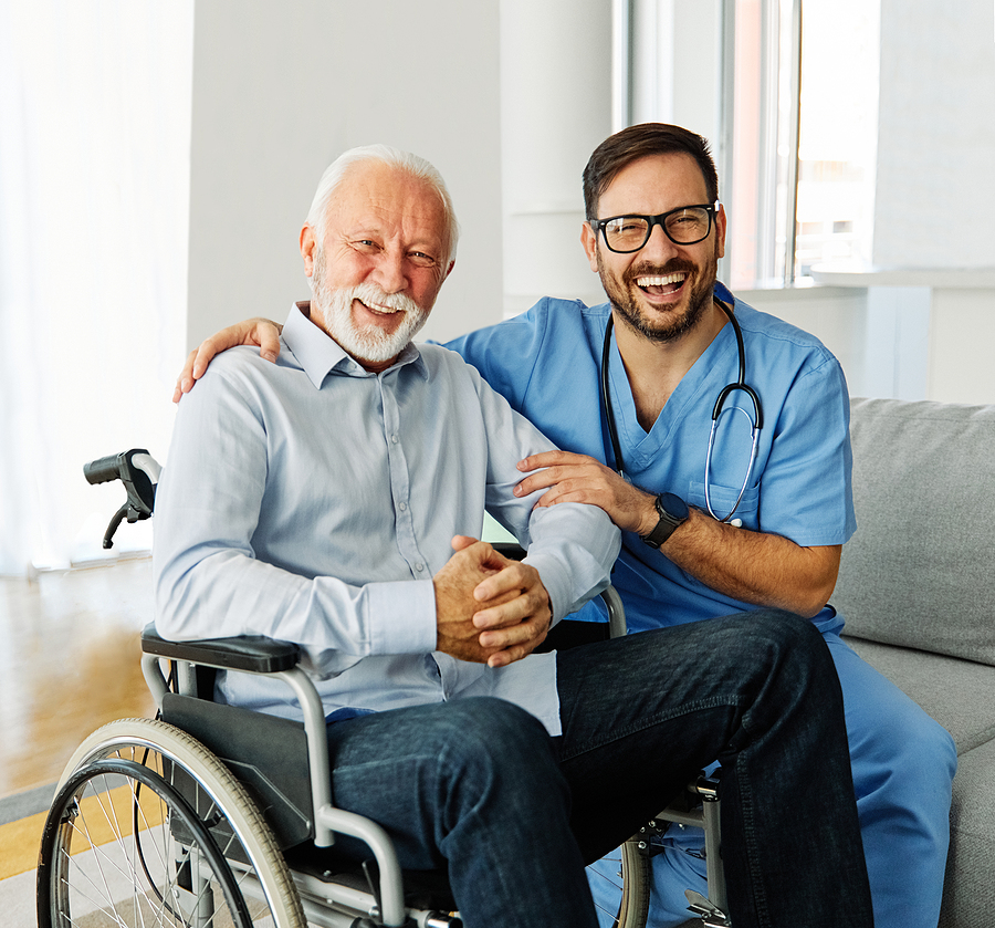male medical assistant kneeling next to elderly male patient in a wheelchair, both smiling for photo