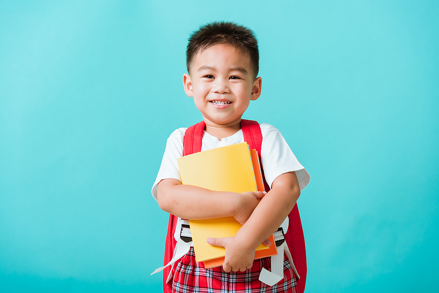 Preschool student wearing a backpack and holding books. 