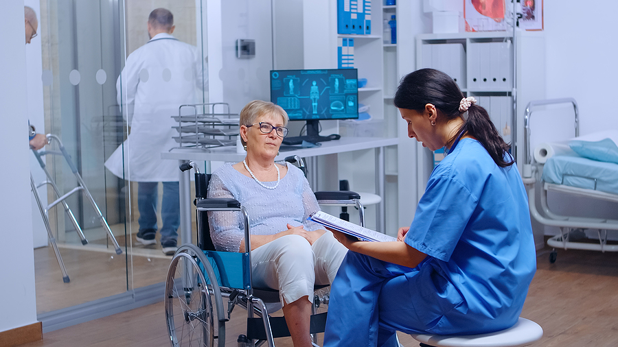 Medical assistant sitting with an elderly patient in a healthcare facility.