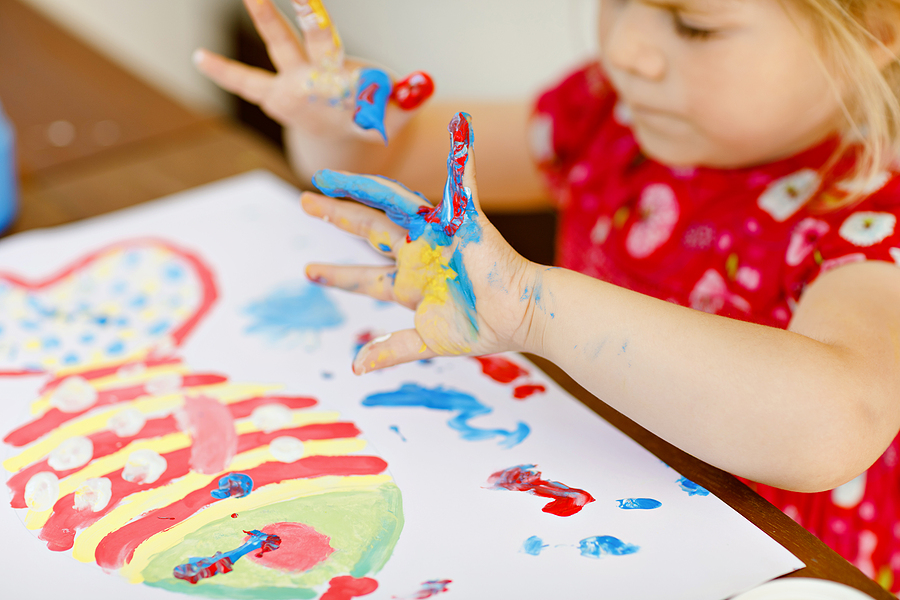 Young preschool student finger painting in a classroom.