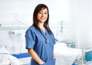 Smiling female medical assistant wearing blue scrubs in a medical exam room. 