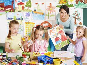 Female preschool teacher working on art projects with a group of young students. 