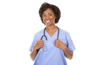 Smiling female medical assistant wearing light blue scrubs with a stethoscope around her neck against a white backdrop. 