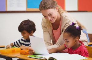 Female teacher helping two young students in a classroom setting. 