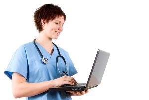 Female medical assistant wearing blue scrubs and holding a laptop. 