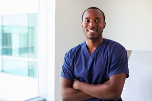 Male medical assistant wearing navy scrubs and smiling at the camera. 