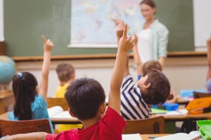 Young students raising their hand in a classroom setting. 