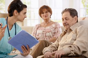 Female medical assistant in scrubs, holding a patient chart and explaining something to a senior couple. 