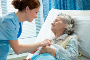 Female medical assistant smiling and assisting an elderly female patient lying in bed. 