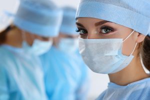 Female surgery assistant wearing a surgical gown and mask and looking at the camera. 