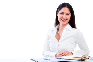 Smiling business woman wearing white blouse while sitting at her desk filling out paperwork. 