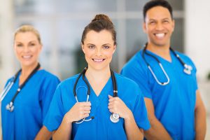 A group of young medical professionals wearing blue scrubs and smiling at the camera. 