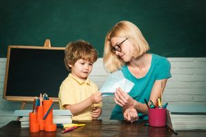 Female preschool teacher helping a young boy with lesson. 