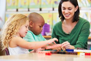 Female teacher helping two young children with an activity. 