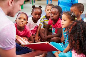 Male teacher reading to a group of young students. 