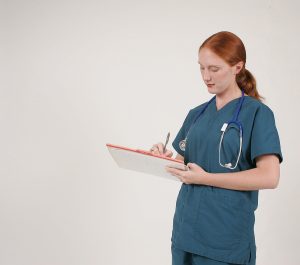 Female medical assistant wearing green scrubs and writing on a clipboard. 