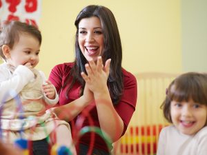 Female early childhood educator smiling and interacting with two young students. 