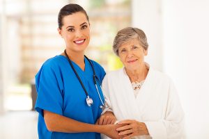 Female medical worker wearing blue scrubs smiling for a photo with an elderly woman. 