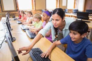 A female teacher helping a group of students at a computer lab. 