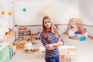 Female early childhood educator standing in a preschool room smiling. 