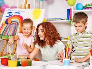 Female preschool teacher painting with two students. 