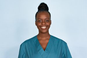 Smiling female medical professional wearing green scrubs against a light blue background. 