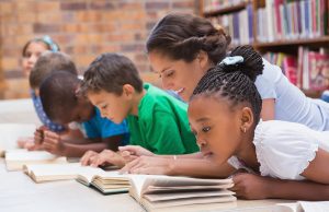 Teacher with young students leaning over books in a library